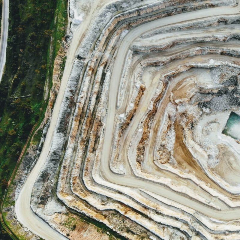 Aerial view of a large, terraced open-pit mine, illustrating the extraction of raw materials needed for electric vehicle batteries.