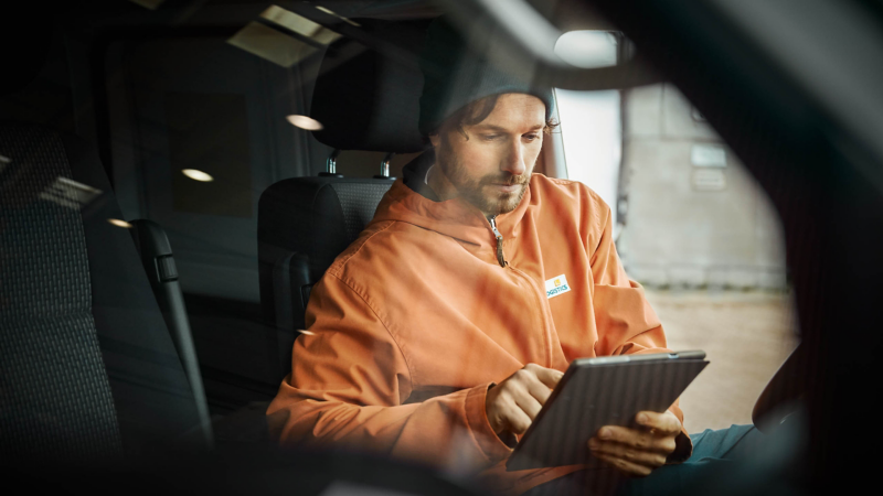 Mann im Volkswagen informiert sich auf Tablet über Leasingratenversicherung.