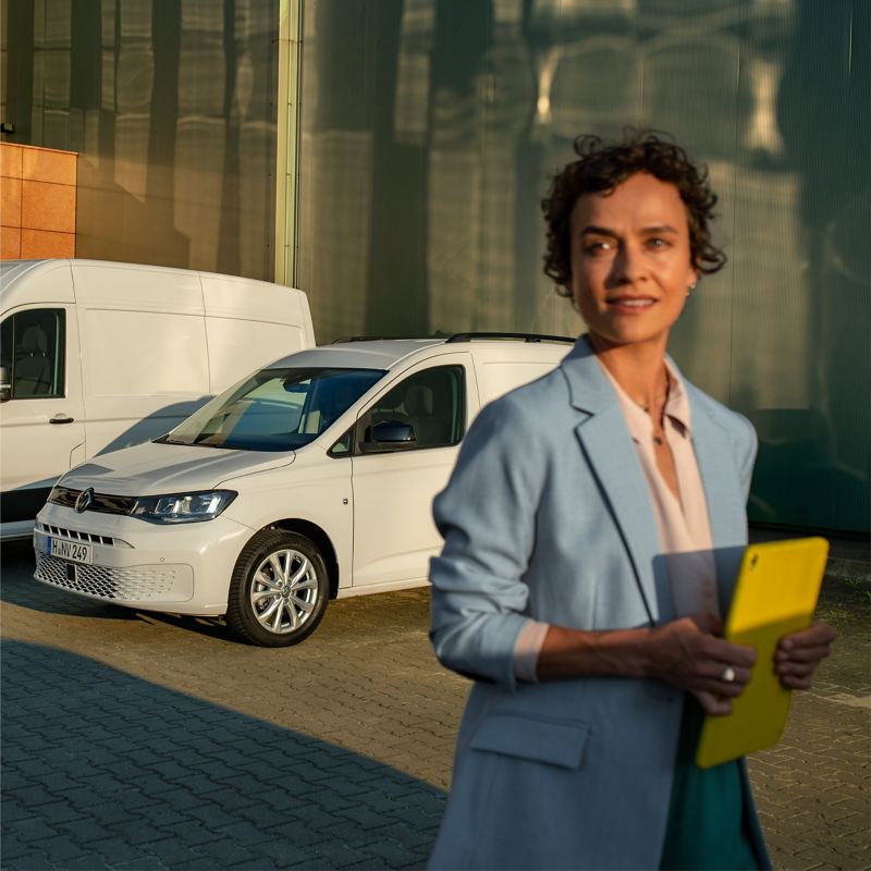 Eine Frau mit Tablet in der Hand steht neben zwei VW Modellen.