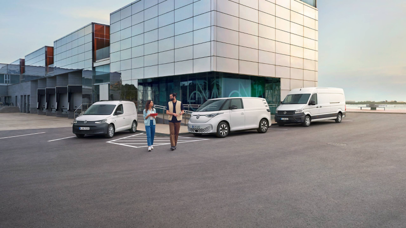 Ein weißer VW Caddy Cargo, ID. Buzz Cargo und Crafter Kastenwagen parken vor einem Bürogebäude, zwei Personen sind herausgekommen.