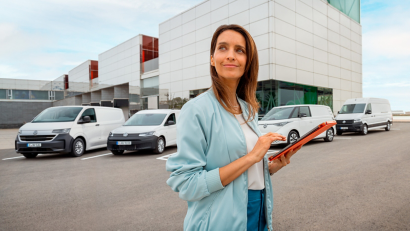 una donna consulta un tablet di fronte a dei veicoli commerciali Volkswagen