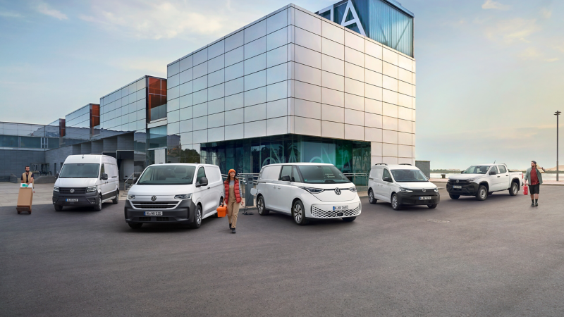 Eine Reihe von fünf verschiedenen weißen Volkswagen Nutzfahrzeugen steht vor einem modernen, verglasten Gebäude, während Personen daneben berufstypischen Tätigkeiten nachgehen.