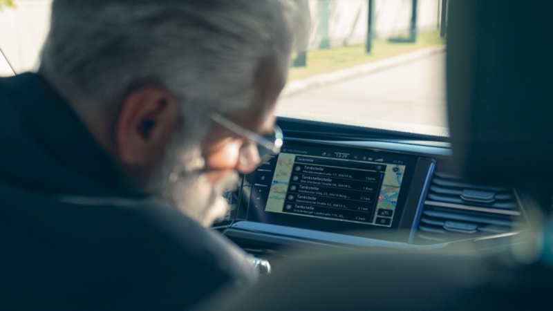 Ein Mann vor den Anzeigen eines Navigationssystems in einem Fahrzeug.