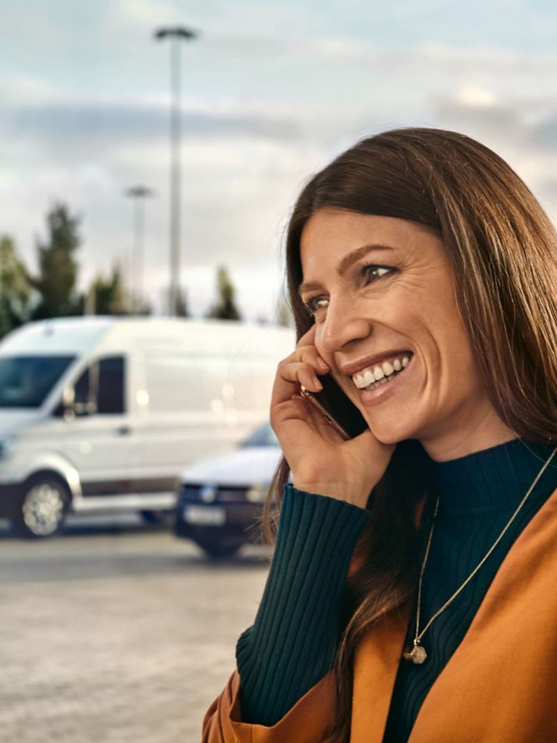 Eine Frau am Telefon, im Hintergrund ihre Flotte von VW Nutzfahrzeuge.