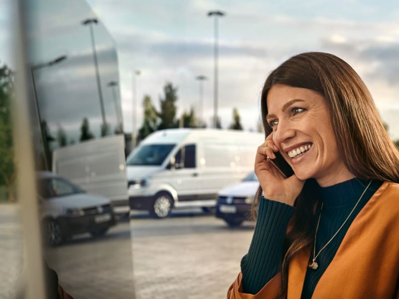 Eine Frau am Telefon, im Hintergrund ihre Flotte von VW Nutzfahrzeuge.