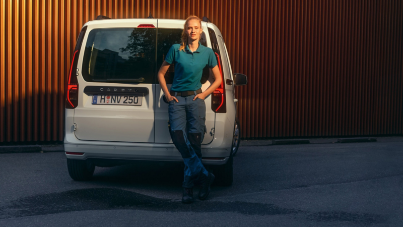 Een vrouw leunt tegen de achterste klapdeuren van de nieuwe Volkswagen Caddy Cargo.