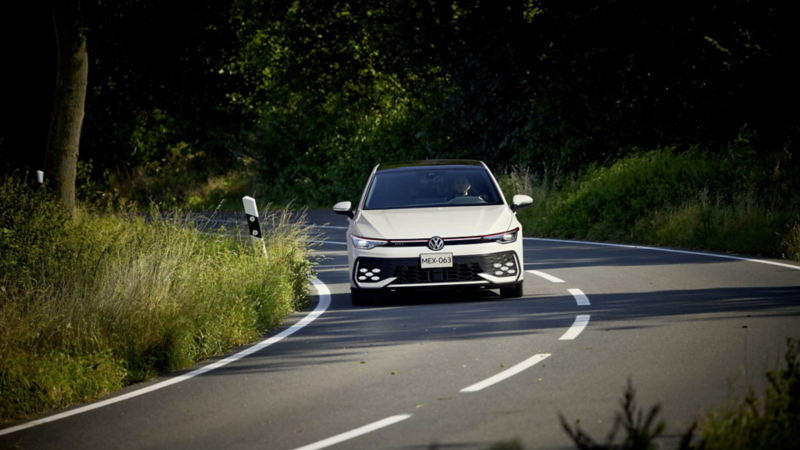 Hombre conduce un GTI 2025 de color blanco, mientras transita por una carretera. 