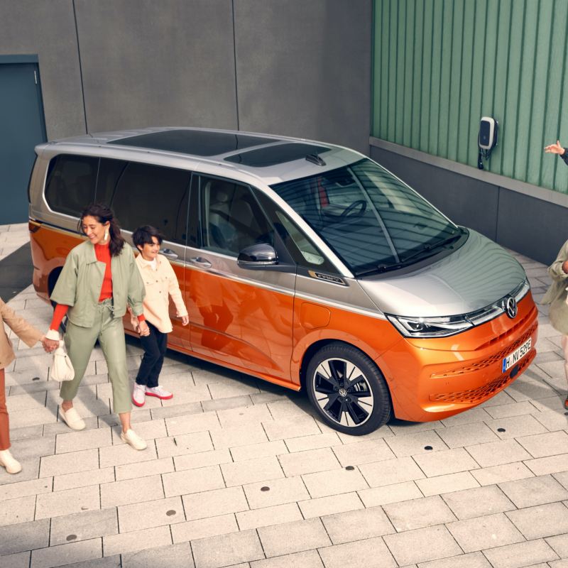 En stor familj går bredvid en VW Multivan 7 eHybrid laddhybrid
