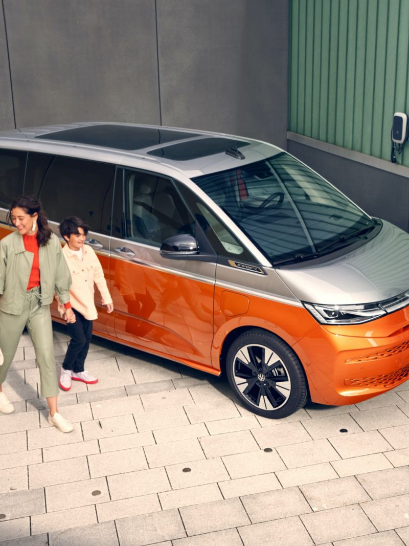 Bildet viser en familie som står og løper rundt den nye Volkswagen T7 Multivan ehybrid ladbar hybrid i orange og grå