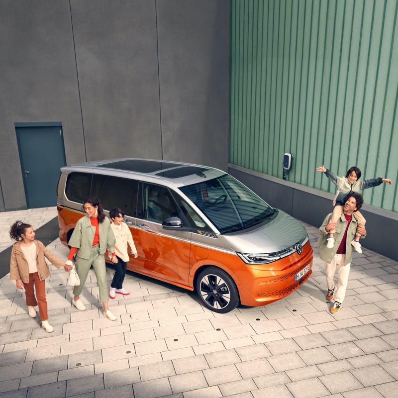 Une famille marche, tout sourire, à côté du VW Multivan Energetic en stationnement.