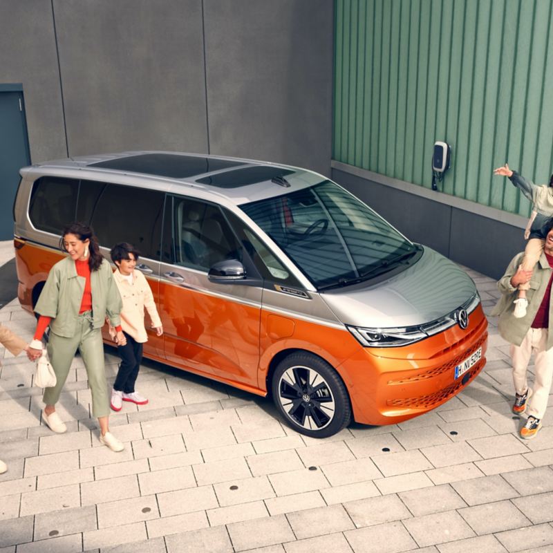 Une famille marche, tout sourire, à côté du VW Multivan Energetic en stationnement.