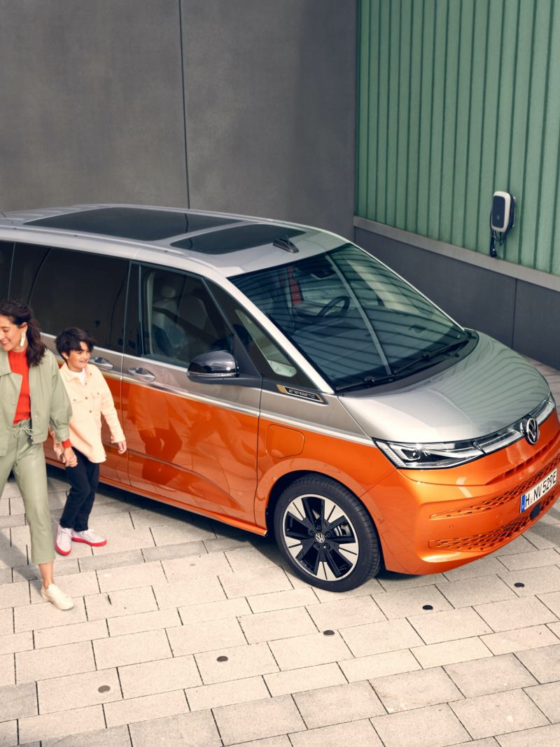 Une famille marche, tout sourire, à côté du VW Multivan Energetic en stationnement.