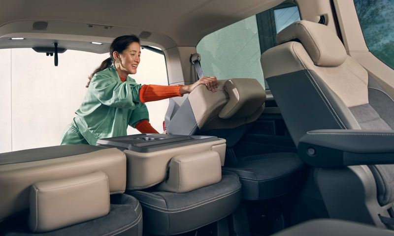 Eine Frau klappt im VW Multivan die Sitze um.