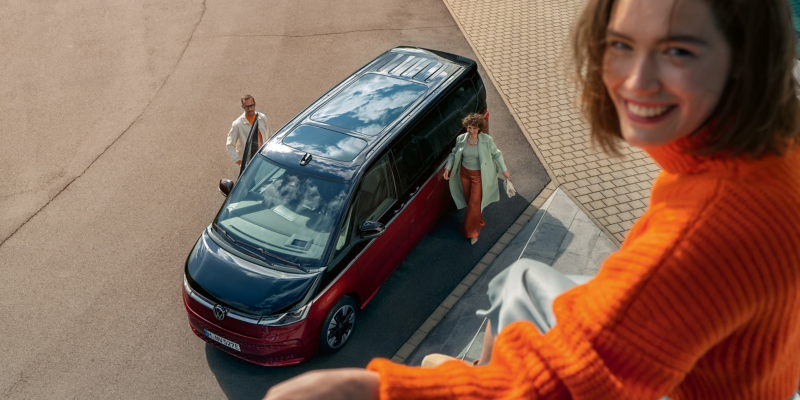 Vue aérienne du VW Multivan rouge et noir avec 2 personnes qui ouvrent les portes et une femme qui observe d'en haut