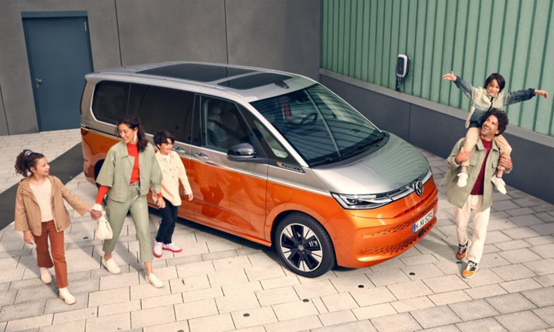 Le Multivan eHybrid de VW est garé dans une cour et une famille marche autour de lui.