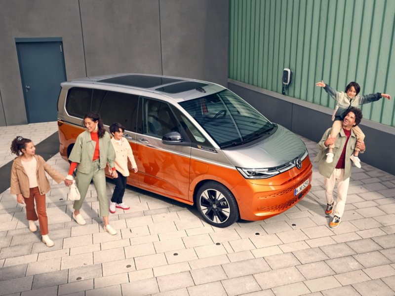 Der VW Multivan eHybrid parkt in einem Hof und eine Familie läuft um ihn herum.