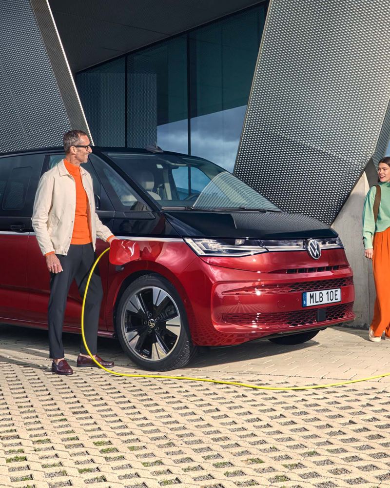 Två personer startar laddningen av en tvåfärgad VW Multivan eHybrid