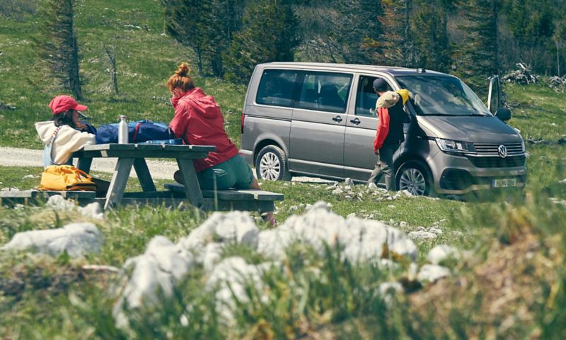 Ein VW Multivan 6.1 steht neben einer Familie beim Picknick.