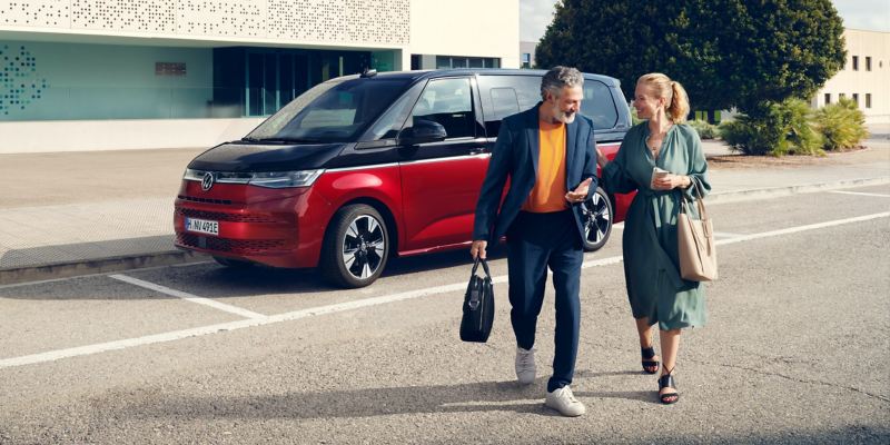 Far och dotter lämnar en tvåfärgad VW Multivan eHybrid parkerad på en väg