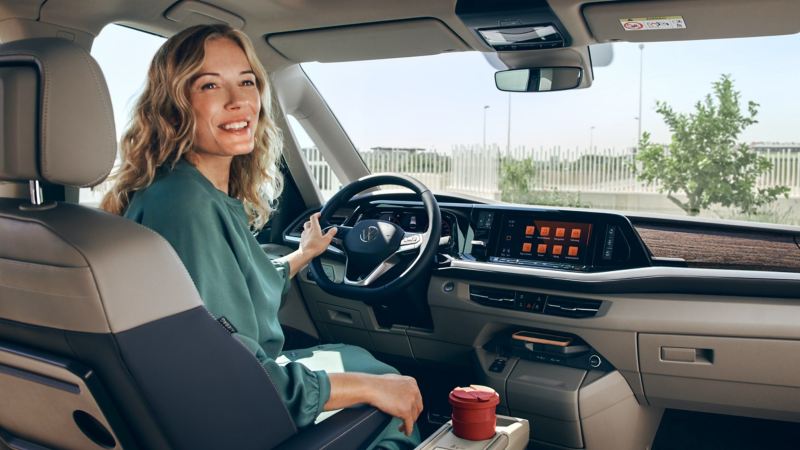 Ein Blick in das Cockpit von der hinteren Sitzreihe eines VW Multivan. Am Steuer sitzt eine Frau.