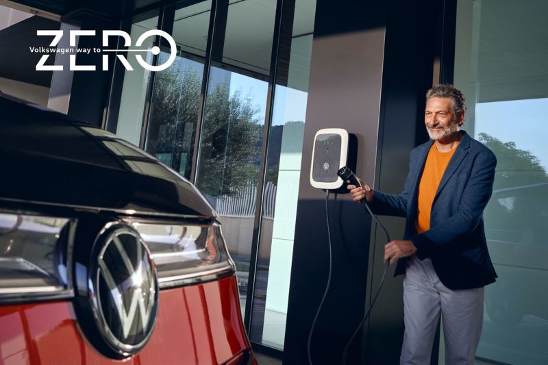 Un homme tient un câble de recharge à la main. Sur la photo, on peut voir la VW Multivan Style.