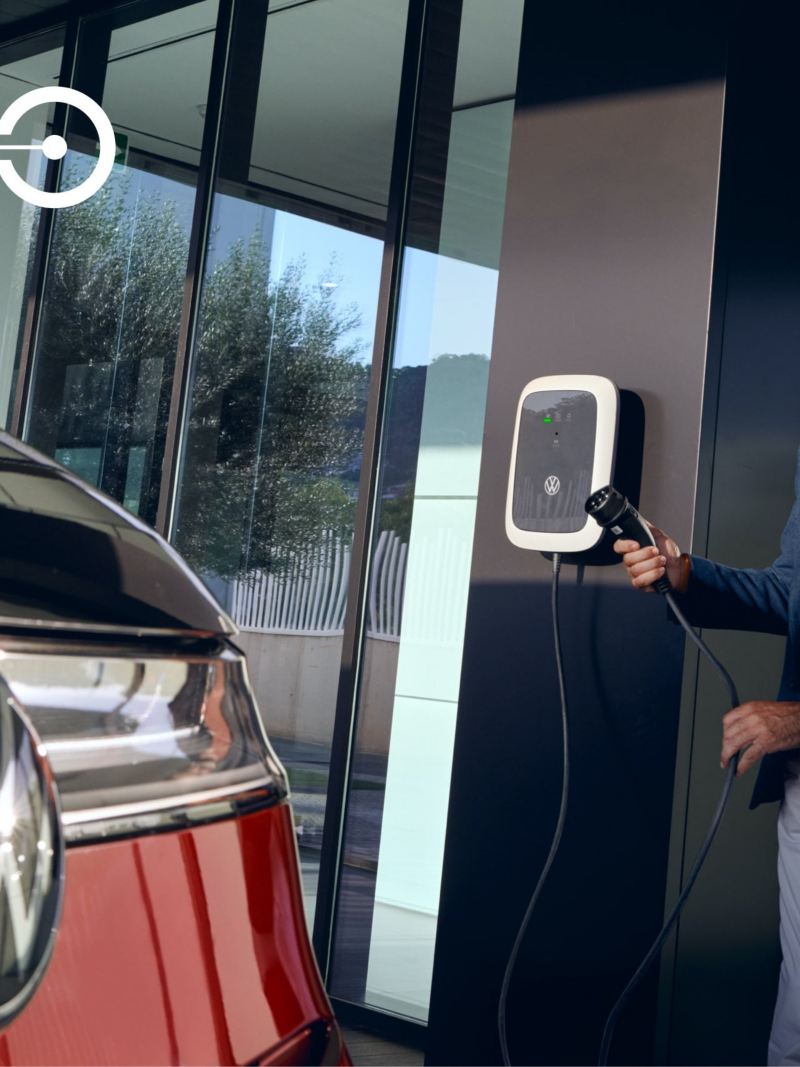 Un homme tient un câble de recharge à la main. La vue en coupe laisse apparaître le VW Multivan Style.