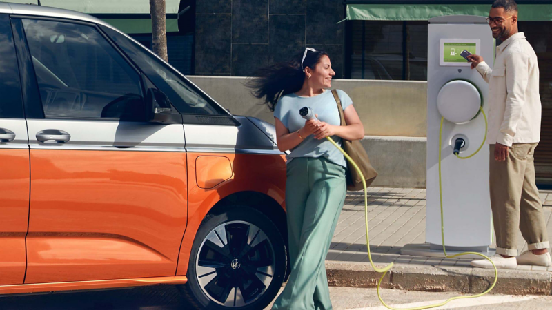 a woman at a public charging point plugging in her ID. Buzz whilst a man pays using a credit card