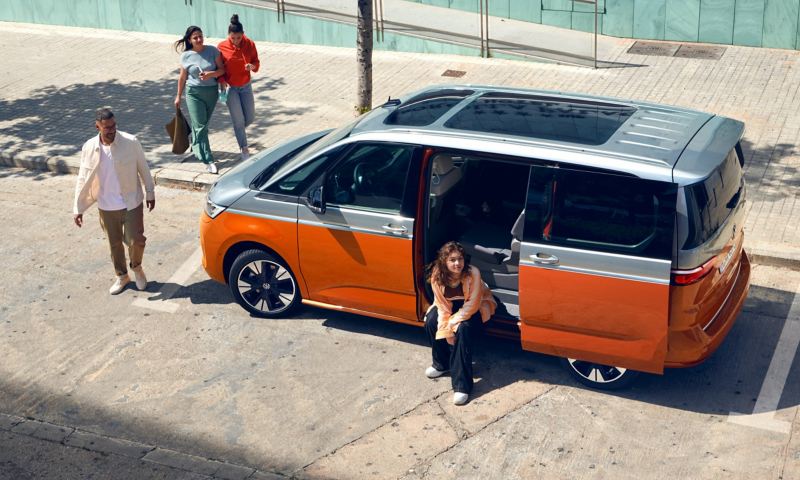 En kvinna sitter i dörrpöppningen på en tvåfärgad VW Multivan Energetic eHybrid med tonat panoramaglastak