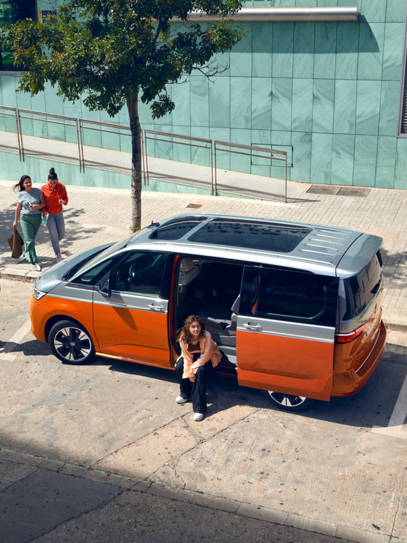 Ein VW Multivan parkt am Straßenrand und eine Frau sitzt an der geöffneten Schiebetür