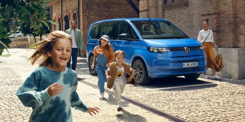 En glad familj vid en blå VW Multivan eHybrid familjebil