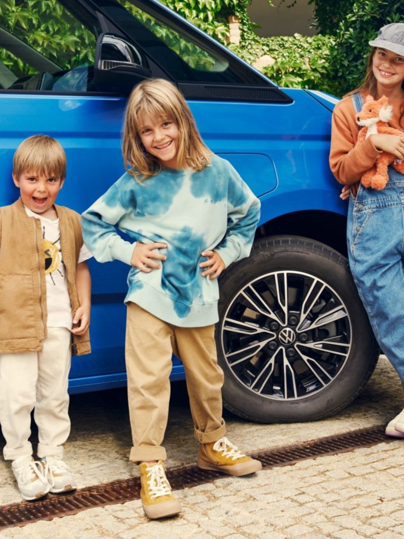 Trois enfants se trouvent devant le Multivan bleu VW.