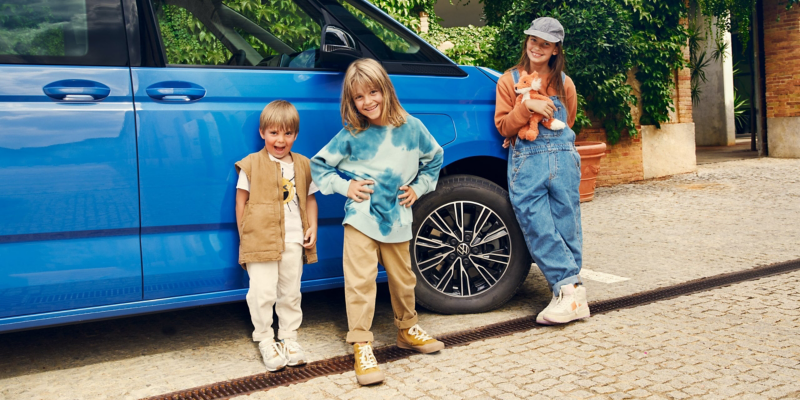Trois enfants se trouvent devant le Multivan bleu VW.