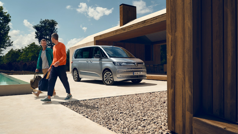 Zwei Männer laufen von einem vor einem modernen Haus parkenden VW Multivan Life weg.