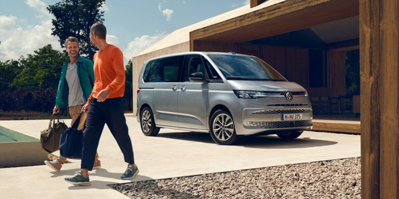 Το VW Multivan Life είναι παρκαρισμένο δίπλα σε ένα κτίριο. Δύο άντρες απομακρύνονται από το αυτοκίνητο κρατώντας τις τσάντες τους.