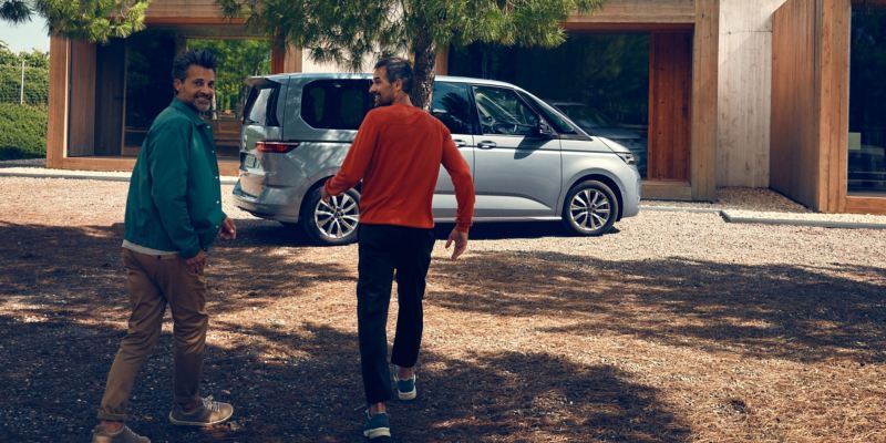 Zwei Männer laufen auf ein parkenden VW Multivan Life zu.