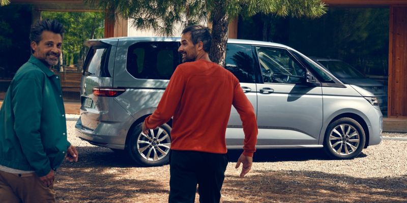 Zwei Männer laufen auf ein parkenden VW Multivan Life zu.