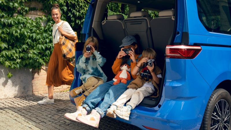 三個小孩坐在一台開著電動尾門的地中海藍New Multivan上