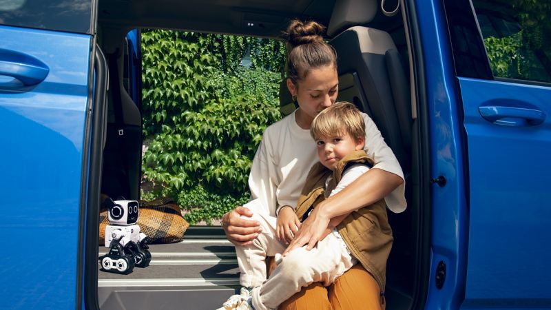 Una donna con un bambino siede nel Volkswagen Multivan aperto.