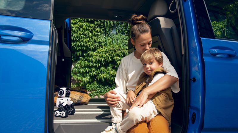 一位媽媽抱著兒子坐在一台地中海藍New Multivan電動側滑門邊