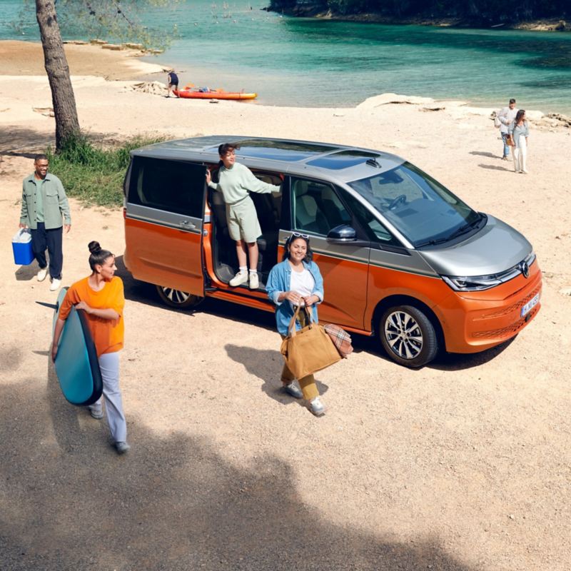Eine Gruppe von Menschen steht neben einem VW Multivan an einem Fluss.