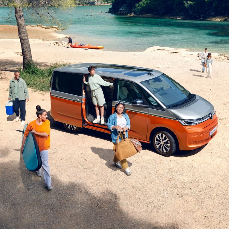 Una famiglia attorno al proprio Volkswagen Multivan parcheggiato in riva a un lago.