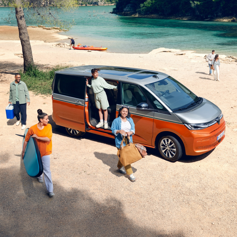 Eine Gruppe von Menschen steht neben einem VW Multivan an einem Fluss.