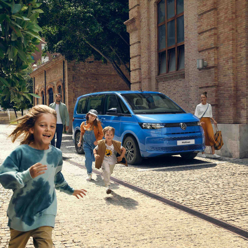 Photo showing a family next to a Multivan parked in a city area.