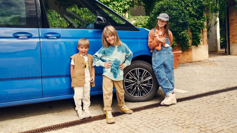 Drei Kinder vor einem VW Multivan.