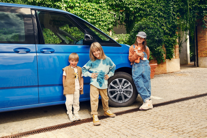 Trójka dzieci stoi na tle prawego boku niebieskiego VW Multivana Family.