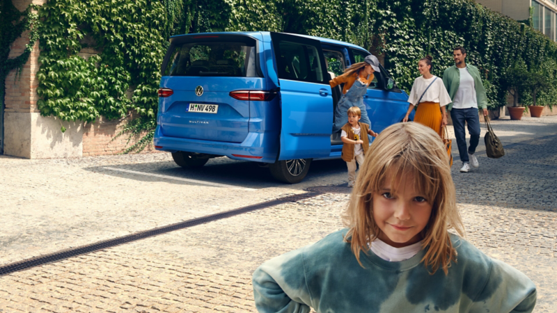 VW Multivan parkt an einer Straße. Um ihn herum Eltern mit zwei Kindern.