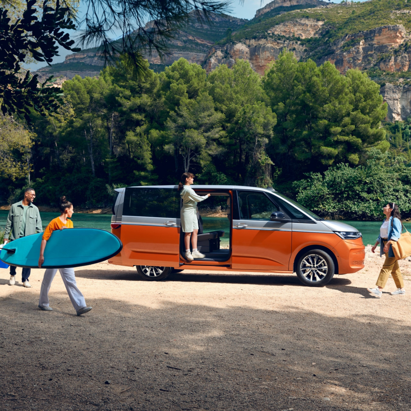 A Multivan parked on a beach with people walking around it