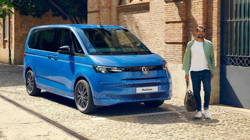 A man walking passed a parked VW Multivan.  