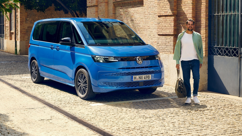 Ein Mann steht neben einem VW Multivan in Medium Blue Metallic.