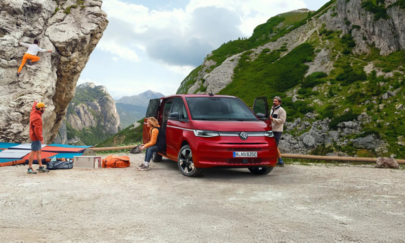 VW Multivan eHybrid stoi podłączony do ładowarki przed kompleksem biurowców.
